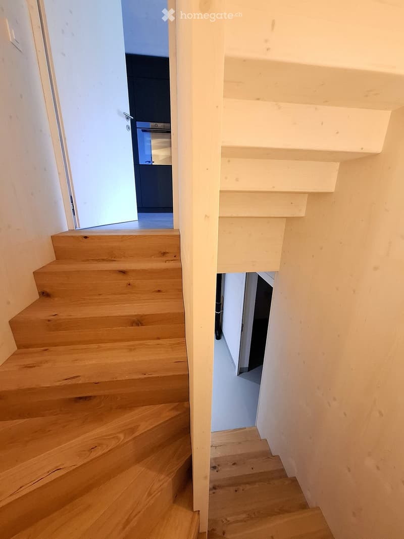 Wooden staircase with white walls and a partially open door leading to another room.