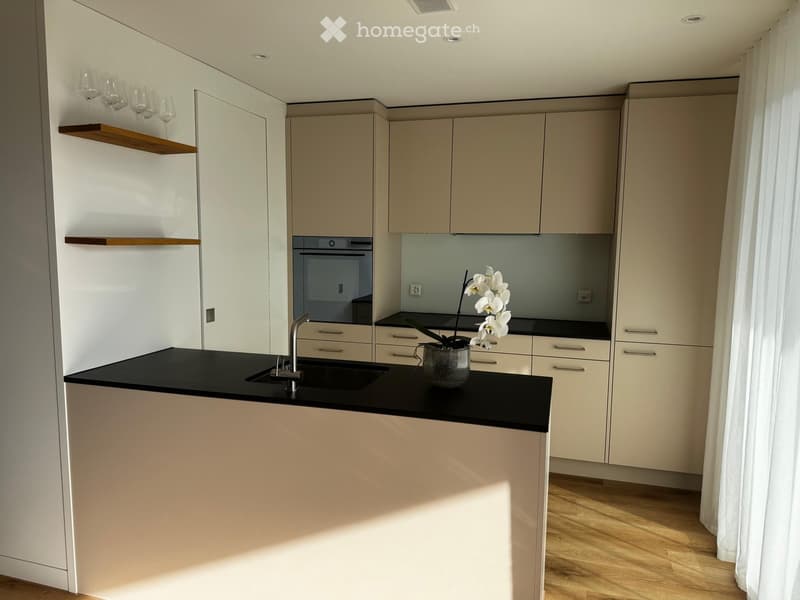 modern minimalist kitchen with white walls, black countertops, stainless steel sink, wine glass shelf, integrated oven, wooden floor, and minimalist cabinetry