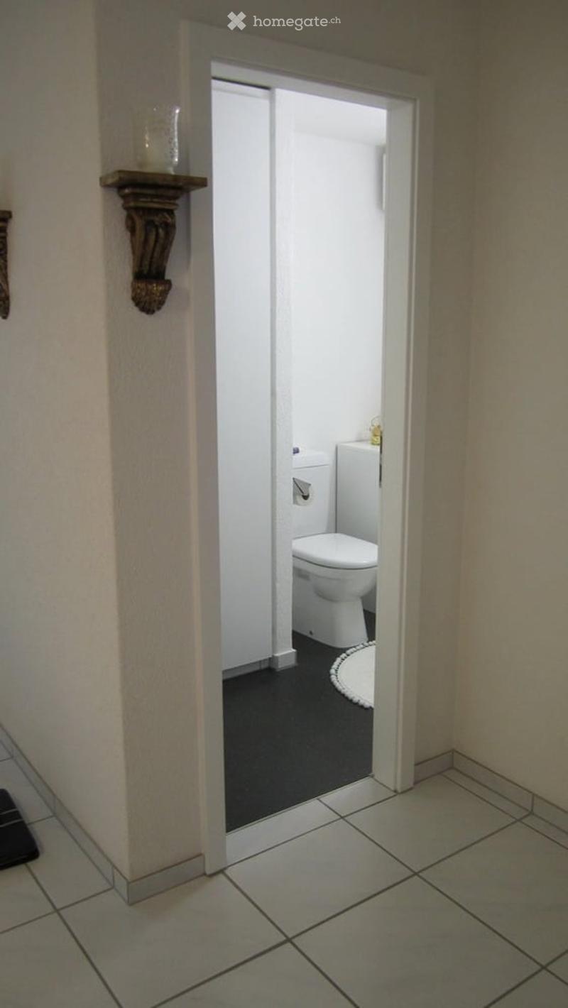 A small bathroom with a toilet, sink, and a round white rug on the floor. The walls are white, and the floor is black.