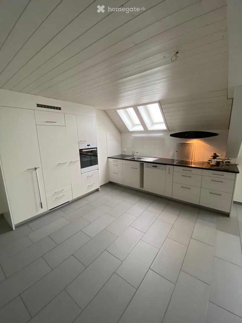 Modern kitchen with white cabinets, stainless steel appliances, and grey tiled floor. Features an oven, sink, dishwasher, and ample storage space.