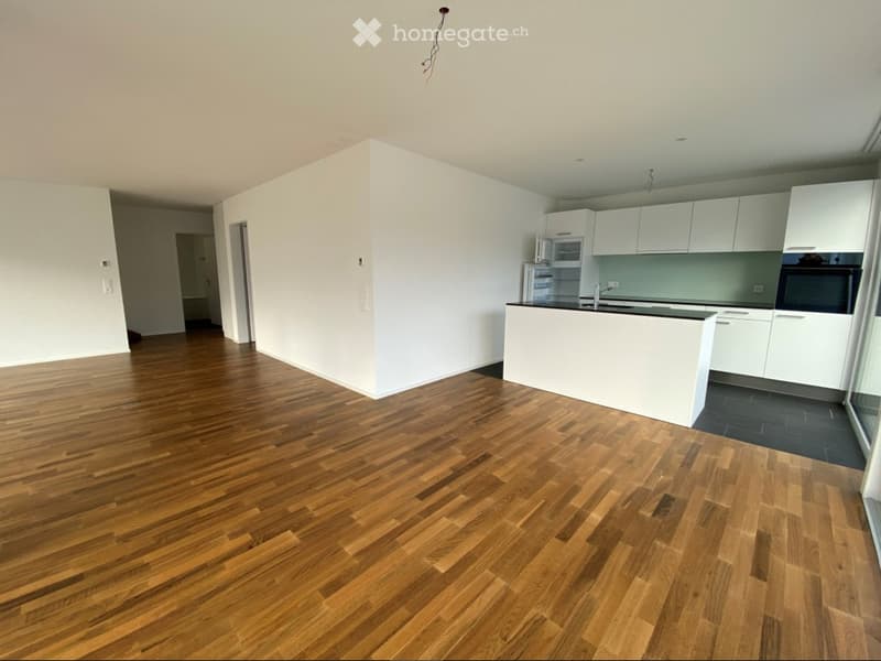 Empty kitchen with white cabinets, a central island, and wooden flooring. No appliances or furniture are present.