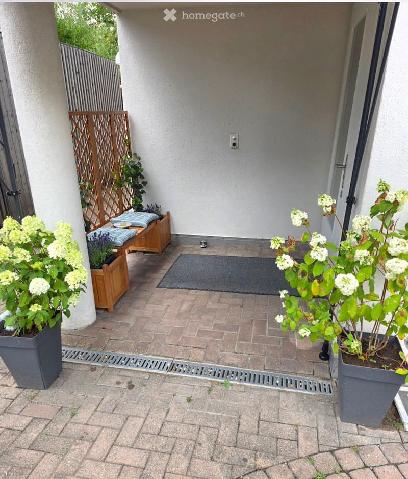 Brick-paved balcony with wooden bench, potted plants, and a wooden lattice screen.