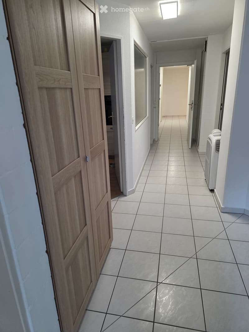 A clean, tiled hallway with white walls, wooden doors, and a small air conditioner unit on the right side.