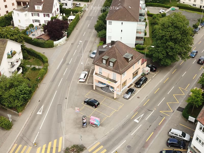 Aerial view of a street with multiple buildings, parking lot, and cars parked in front of a building
