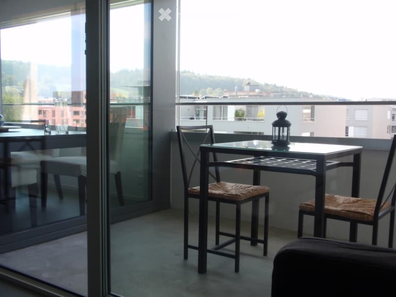 Balcony with a small table and two chairs, overlooking a cityscape with buildings and greenery.