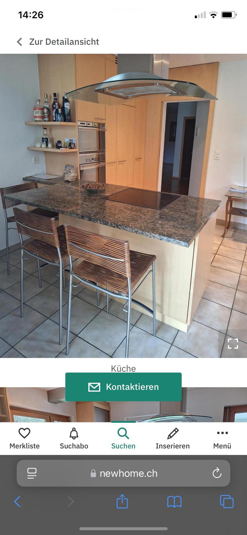 Modern kitchen with granite countertop, built-in stove, oven, and wooden cabinets. Two wicker chairs are placed at the counter.