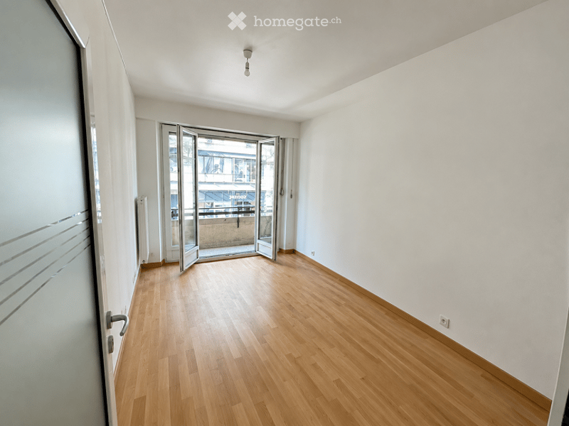 Empty room with wooden flooring, white walls, and large sliding glass doors leading to a balcony.