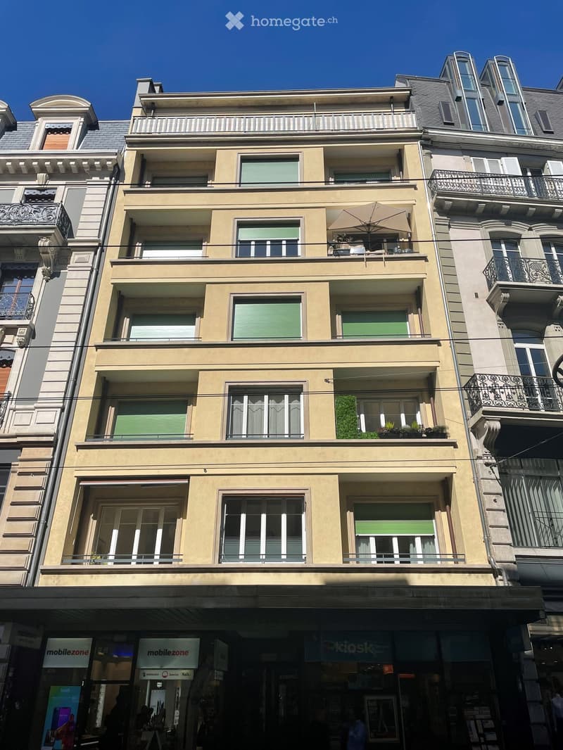 Four-story residential building with multiple balconies, large windows, and decorative railings. The ground floor features commercial storefronts with signage for 'mobilezone'.