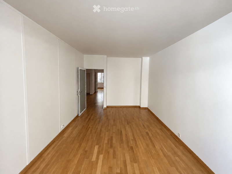 Empty hallway with light wooden flooring and white walls, featuring a single door at the end.
