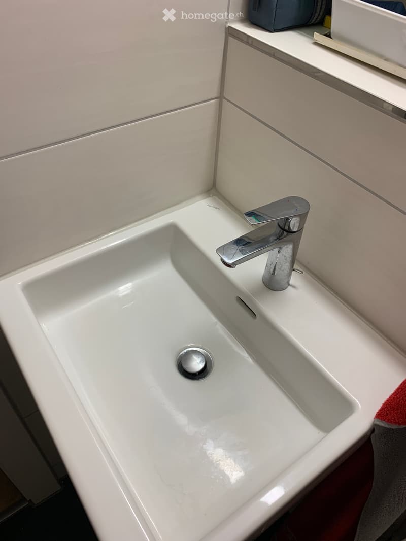 Modern white sink with a sleek chrome faucet, mounted on a white countertop with a subtle gray towel visible on the right side.