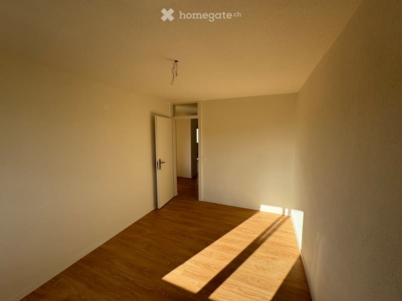 Empty hallway with wooden flooring, light-colored walls, and a partially open door leading to another room.