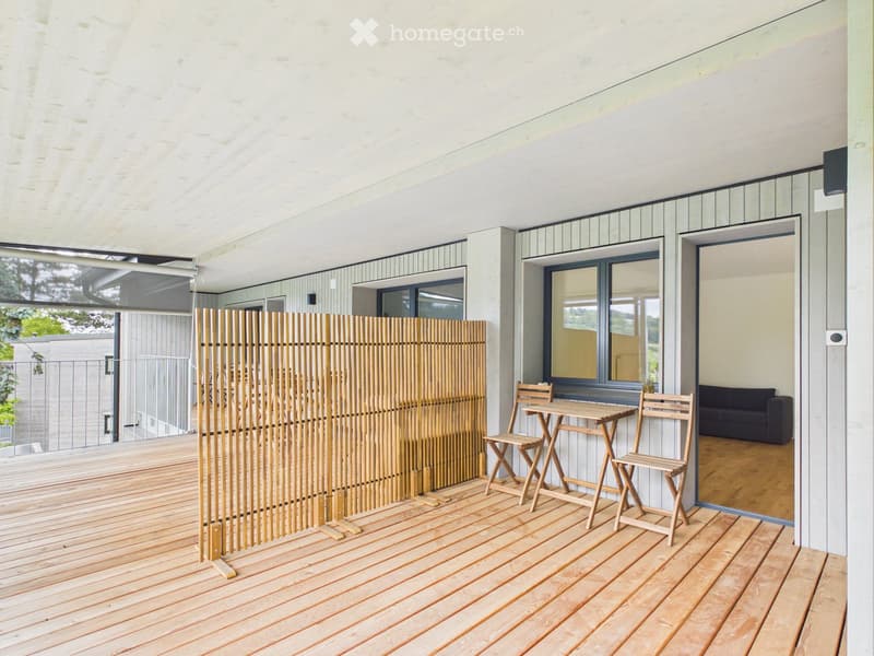 Wooden deck with a bamboo screen, small table, and chairs, with a view of the living room inside.