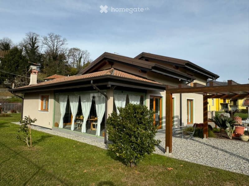 Single-story house with a tiled roof, large windows, and a covered outdoor patio area with furniture.