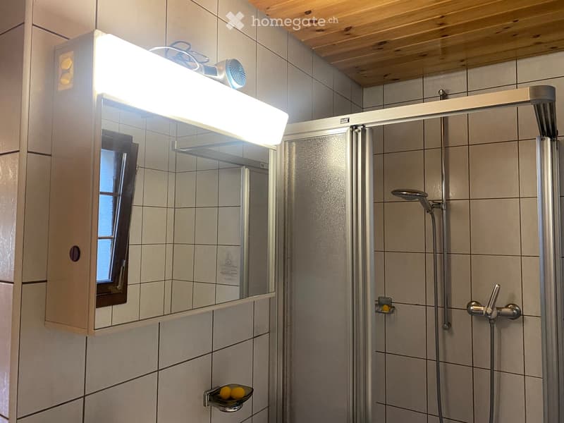 Modern bathroom with a large mirror, built-in light fixture, shower with multiple heads, and a small window for natural light.