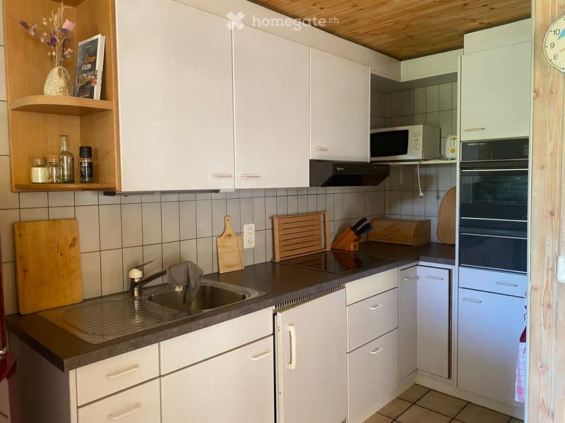 Modern kitchen with white cabinets, stainless steel sink, oven, microwave, and wooden shelves holding decorative items and jars.