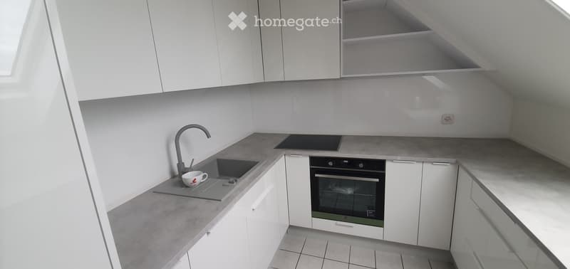 Modern kitchen with white cabinets, grey countertops, built-in oven, and a sink with a faucet. A cup is placed on the counter.
