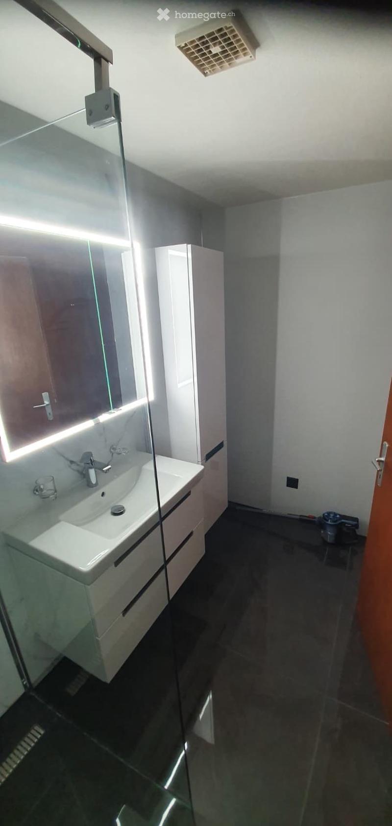 Modern bathroom with a white sink, mirrored cabinet, and sleek black tiled floor.