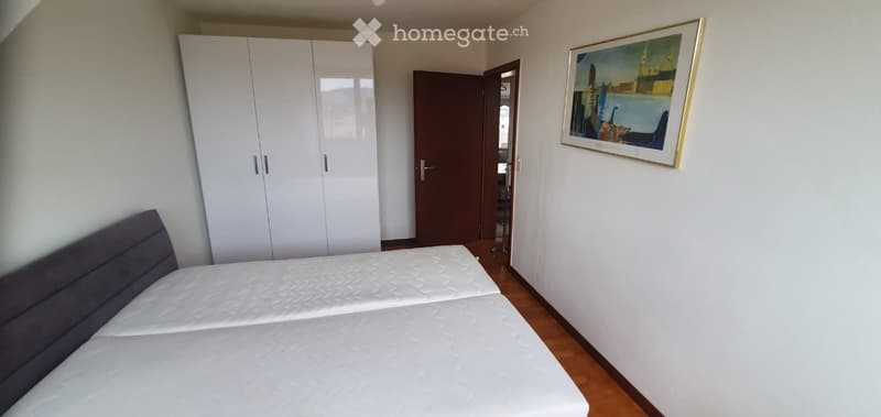 Bedroom with a double bed, white wardrobe, and a framed picture on the wall. The room has wooden flooring and white walls.