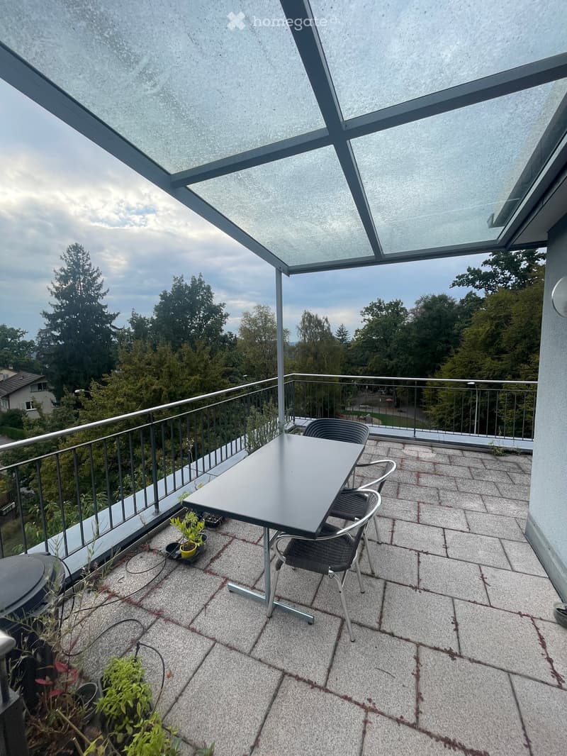Balcony with a glass roof, tiled floor, metal railing, and a small table with chairs.