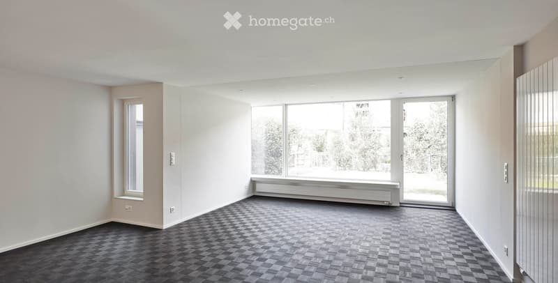 Empty room with light-colored walls, dark checkered flooring, large windows, and a sliding glass door leading outside.