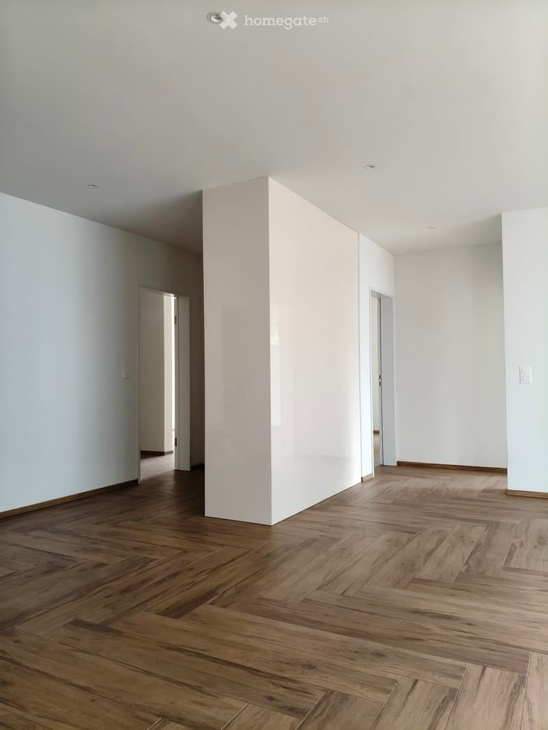 Empty hallway with wooden flooring and white walls, featuring recessed ceiling lights and two open doorways leading to other rooms.
