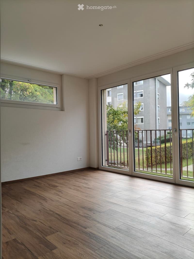 Empty room with wooden flooring, large sliding glass doors leading to a balcony, and a window on the left side.