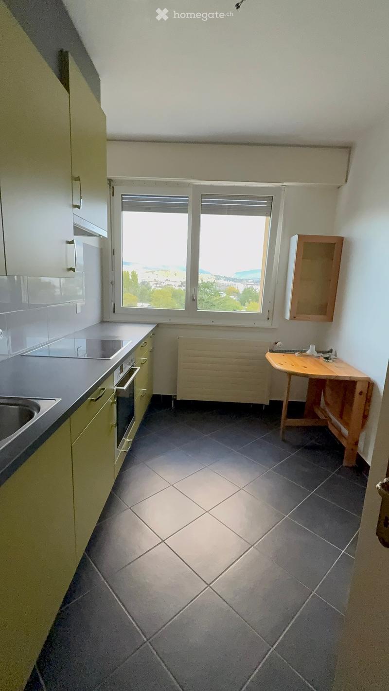 Empty kitchen with light green cabinets, dark tiled floor, and a window overlooking a cityscape. No appliances or furniture are present.