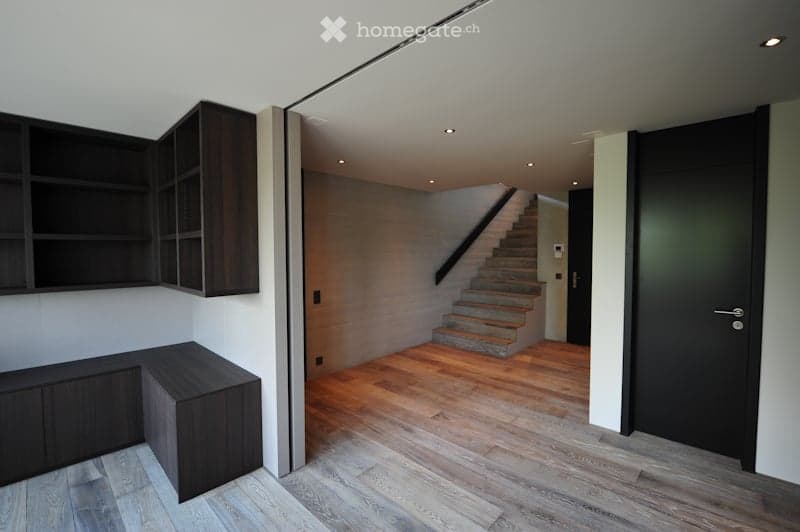 Modern hallway with wooden flooring, built-in dark wooden shelving units, and a staircase leading to an upper level.