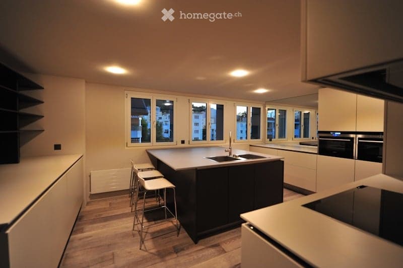 Modern kitchen with white cabinets, dark kitchen island, stainless steel appliances, and bar stools.