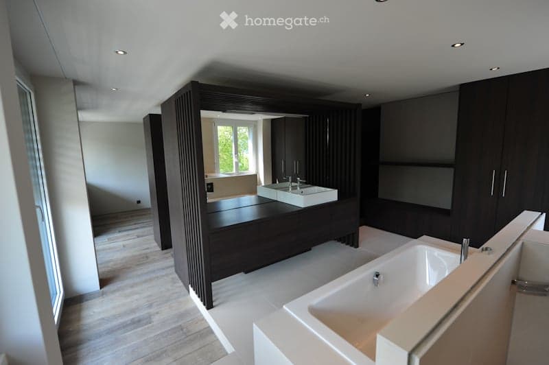 Modern bathroom with dark wood cabinets, white sink, bathtub, and large mirror. The space features recessed lighting and a sleek design.