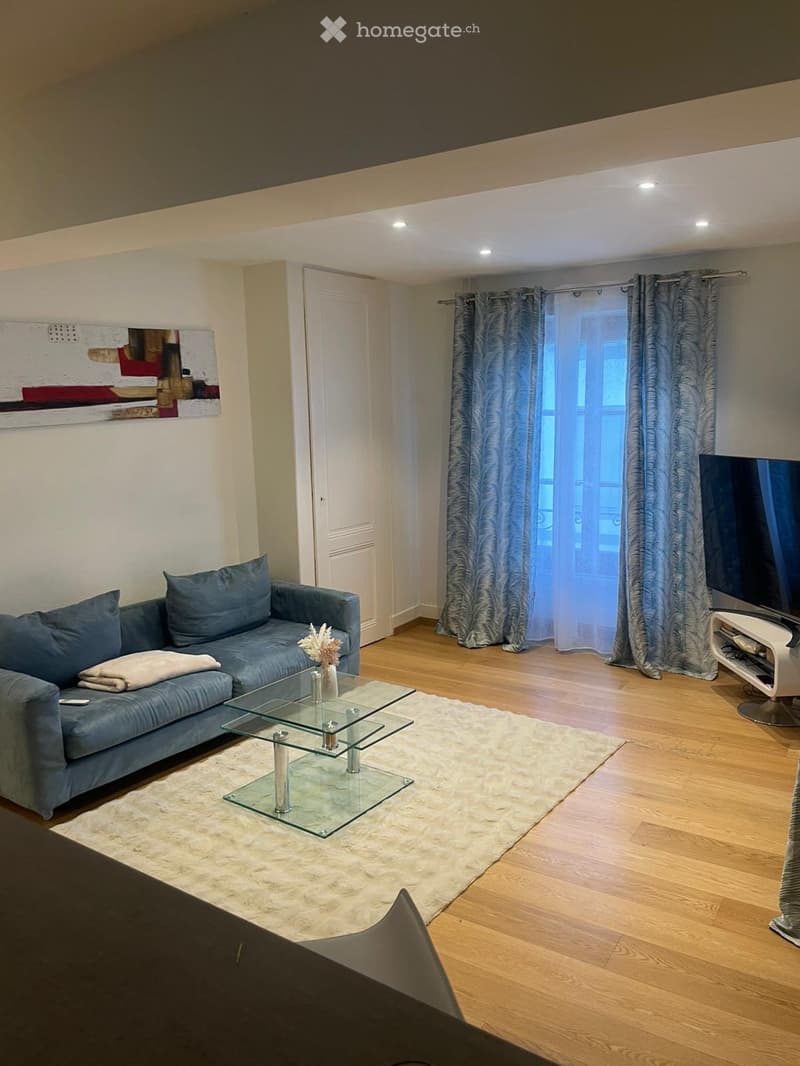 Modern living room with a blue sectional sofa, glass coffee table, white shag rug, TV stand, and decorative vase on the coffee table.