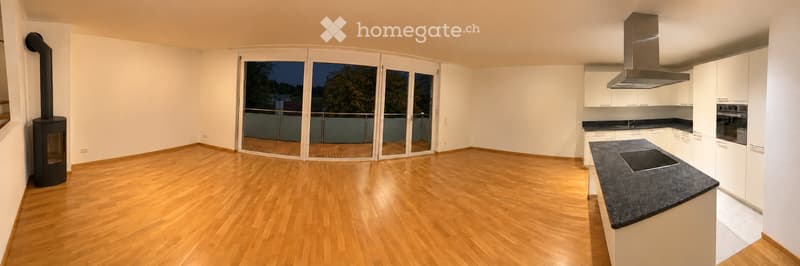 Open-plan space with a modern kitchen area and a living area, featuring light wooden flooring, white cabinetry, a stainless steel range hood, and large glass doors leading to a balcony.