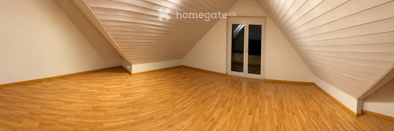 Empty attic room with wooden flooring, white walls, and a large window with glass panels.