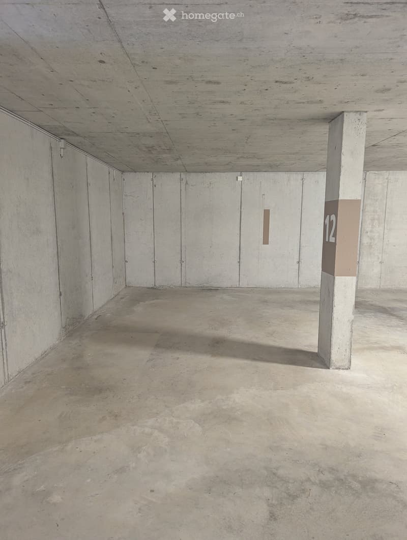 Empty underground garage with concrete walls, floor, and ceiling. A single pillar and a numbered sign are visible.
