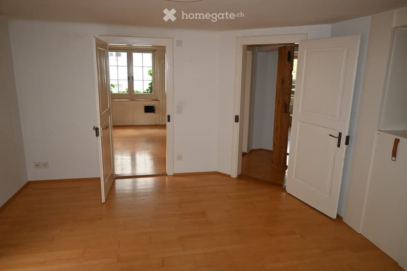 Empty hallway with wooden flooring, white walls, and open doors leading to adjacent rooms. No furniture or equipment visible.