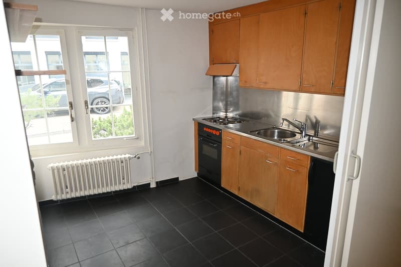 Modern kitchen with wooden cabinets, stainless steel sink, oven, and black tiled floor.