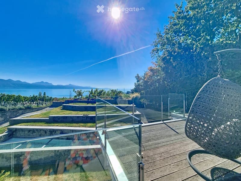 A modern outdoor deck with glass railings, wooden flooring, and a scenic view of a lake and mountains in the background.
