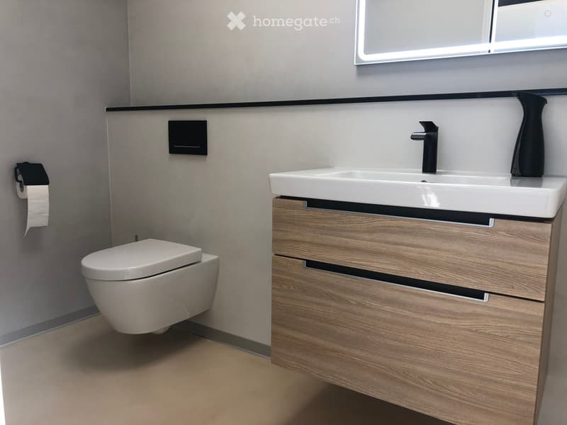 Modern bathroom with a white toilet, wooden vanity with a sink, and a black faucet. Toilet paper holder is mounted on the wall.