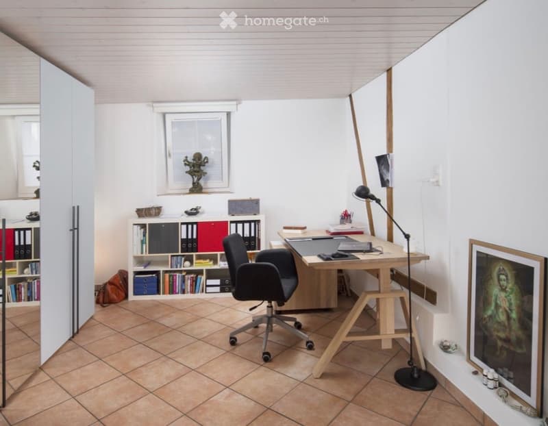 Modern office space with a wooden desk, ergonomic chair, bookshelf, and a large window providing natural light.
