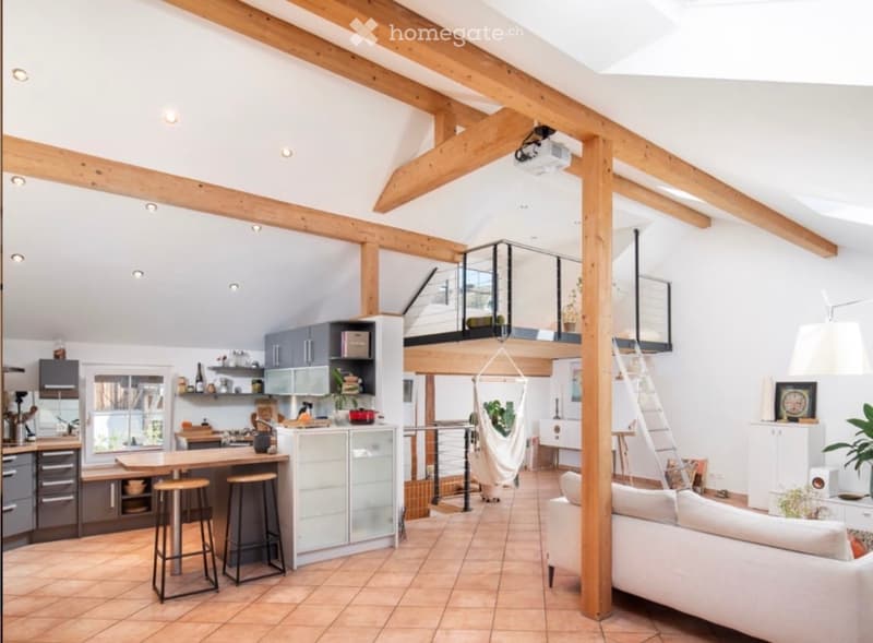 Open-plan living and dining area with exposed wooden beams, a white sofa, a coffee table, a kitchen island with stools, and a hanging hamock in the background.