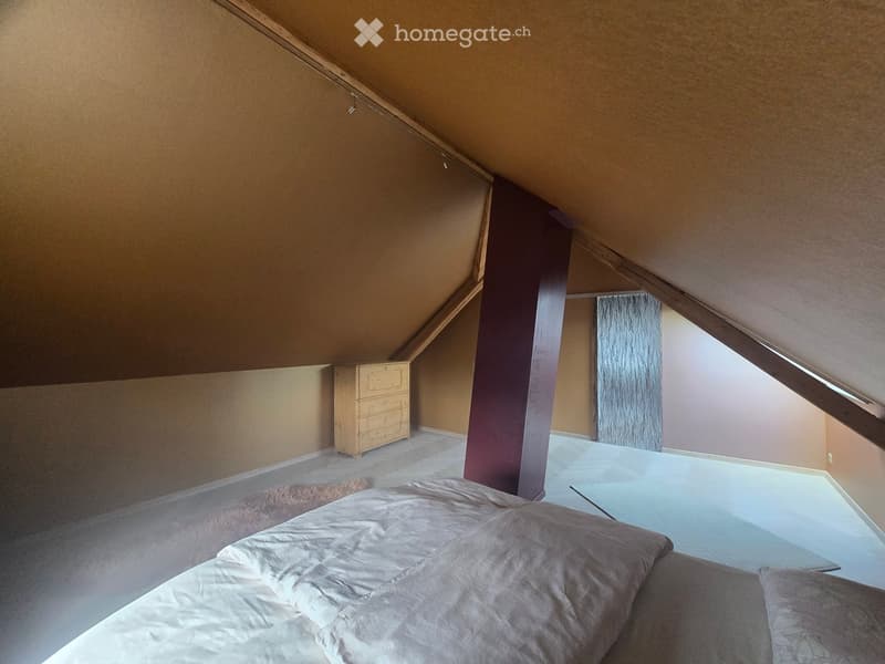 Cozy attic bedroom with slanted wooden ceilings, a neatly made bed, a wooden dresser, and a small rug.