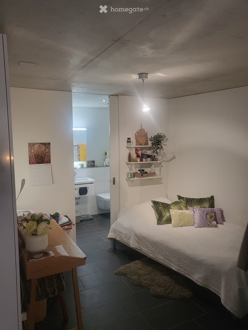 Cozy bedroom with a neatly made bed, nightstand, shelves, and a small adjacent bathroom.