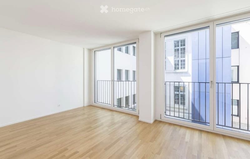 Empty room with wooden flooring, large windows, and sliding glass doors leading to balconies.