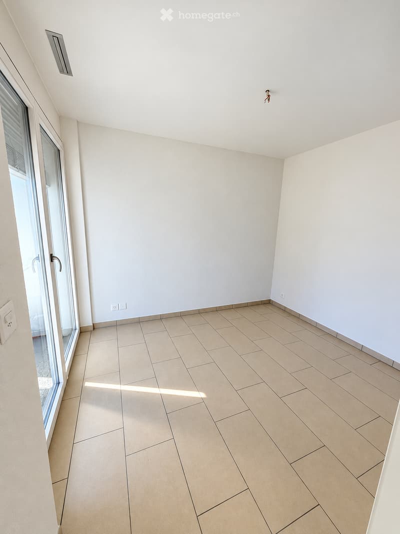 Empty room with tiled floor and white walls, featuring a large glass door leading outside.