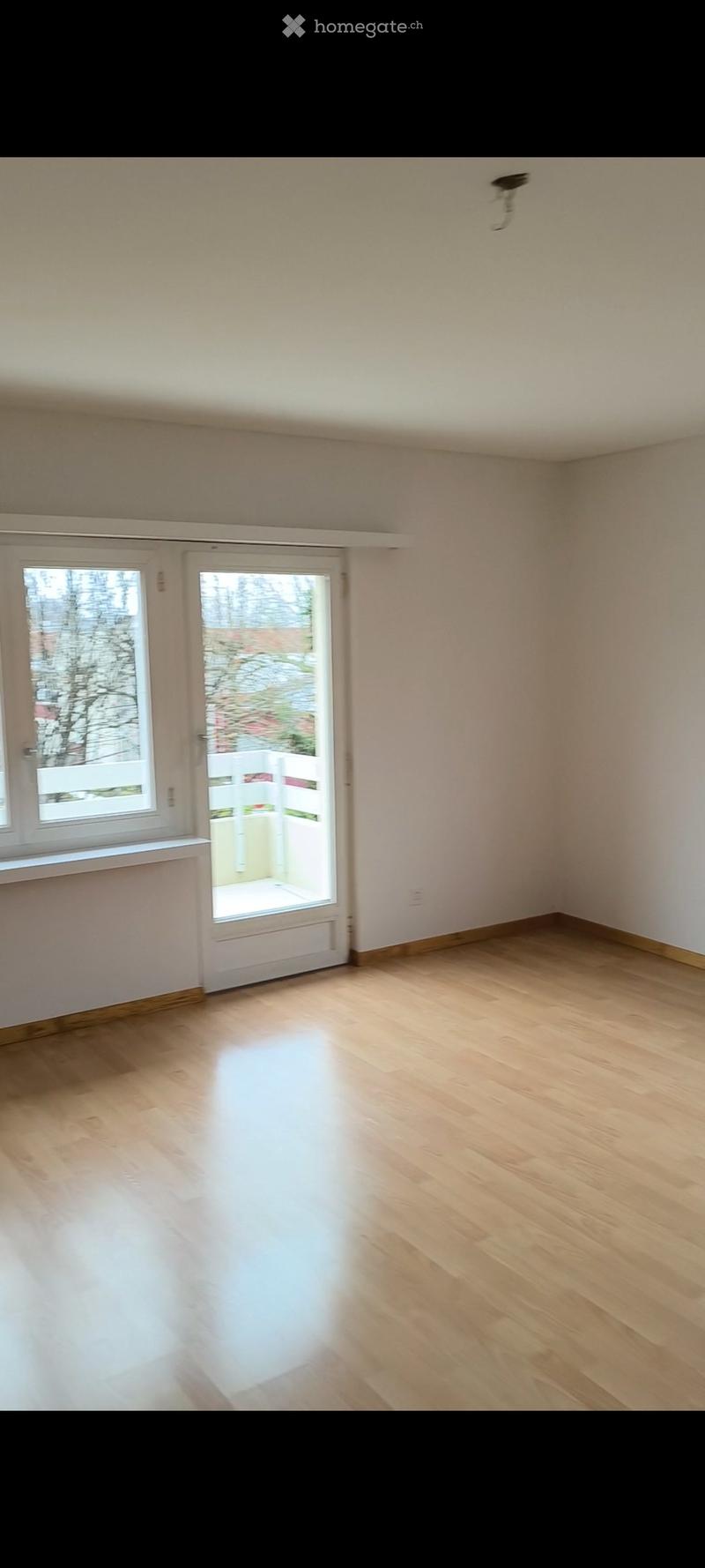 Empty room with light wooden flooring, white walls, and large windows and a door leading to an outdoor area.