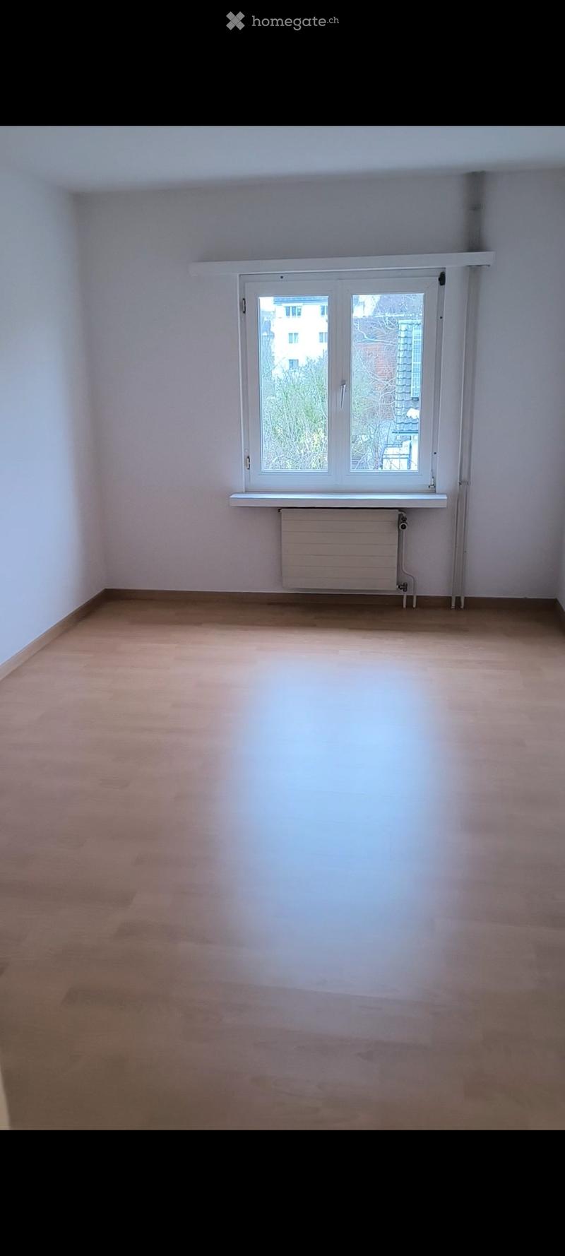 Empty room with wooden flooring, white walls, and a window with a radiator below it.