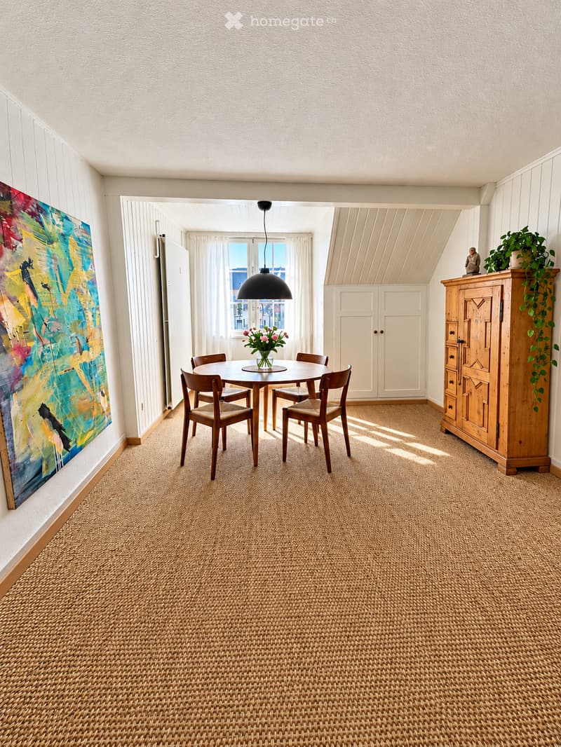 Dining room with a round wooden table, four chairs, a large wooden cabinet, a colorful painting on the wall, and a potted plant on top of the cabinet.