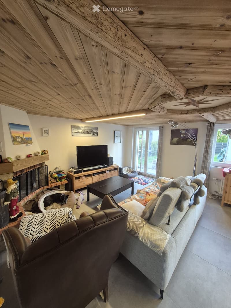 Living room with exposed wooden beams, fireplace, sofa, coffee table, television, dog bed, and armchairs.