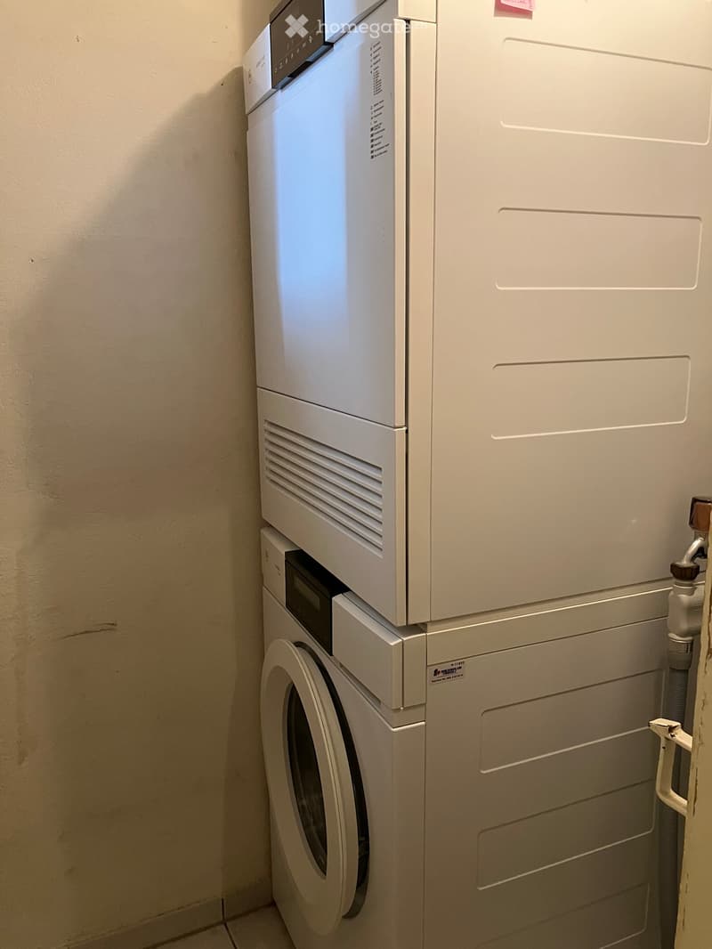 A compact laundry area featuring a stacked washing machine and dryer unit against a beige wall.