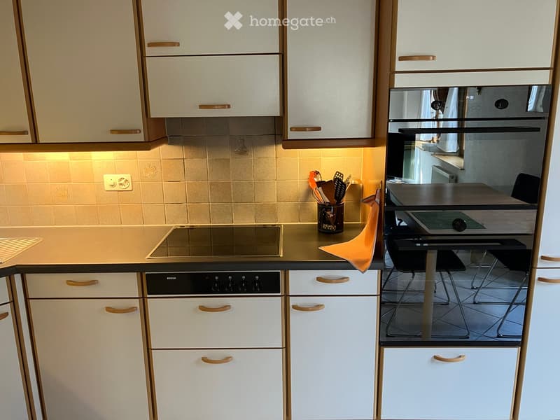 Modern kitchen with white cabinets, stainless steel appliances, and a sleek countertop. Features a built-in oven, stove, and a small dining area with a table and chairs.